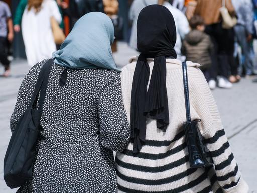 Zwei muslimische Frauen mit Kopftuch gehen in Düsseldorf auf der Straße Arm in Arm.