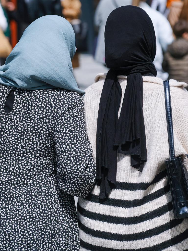 Zwei muslimische Frauen mit Kopftuch gehen in Düsseldorf auf der Straße Arm in Arm.