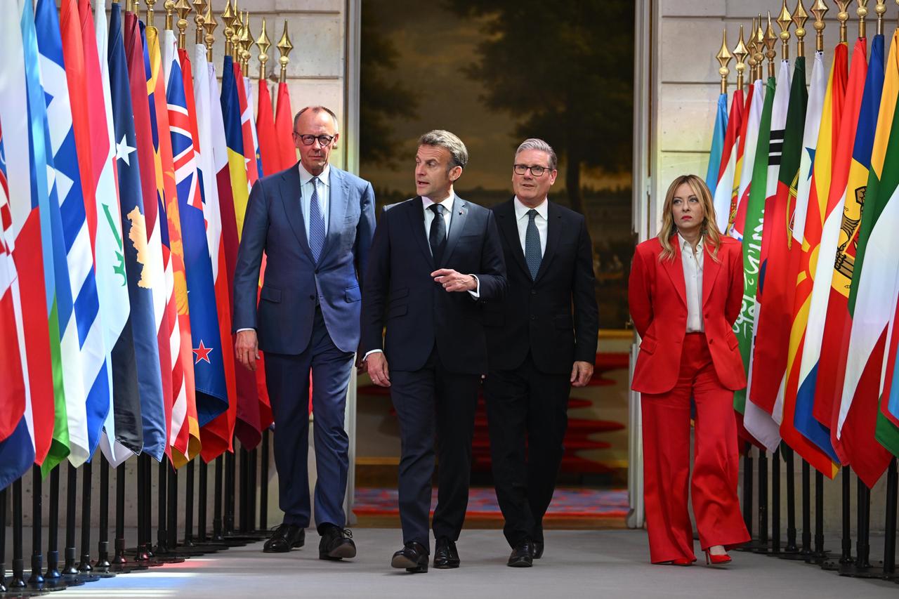 Drei Männer und eine Frau schreiten entlang verschiedener Flaggen.