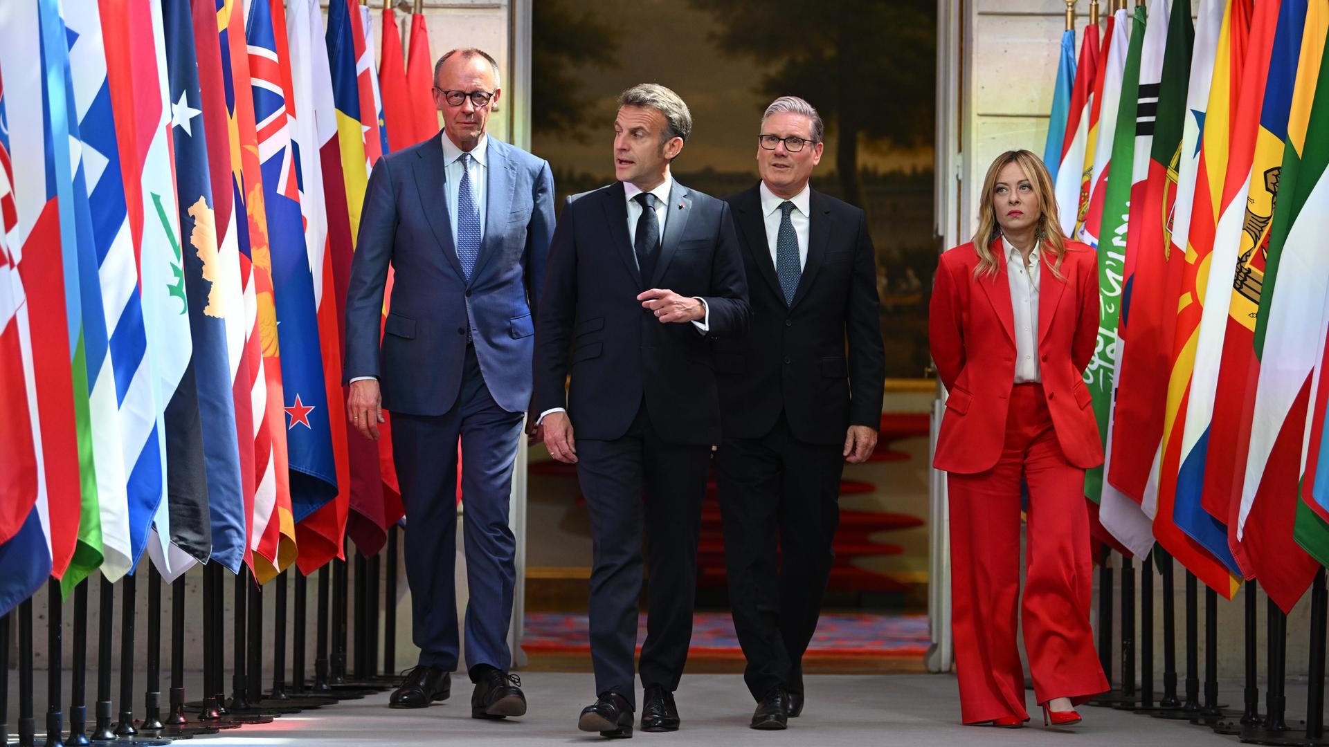 Drei Männer und eine Frau schreiten entlang verschiedener Flaggen.