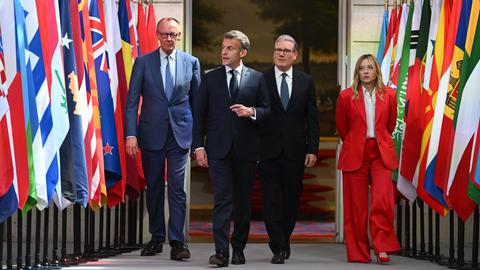 Drei Männer und eine Frau schreiten entlang verschiedener Flaggen.