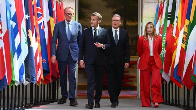 Drei Männer und eine Frau schreiten entlang verschiedener Flaggen.