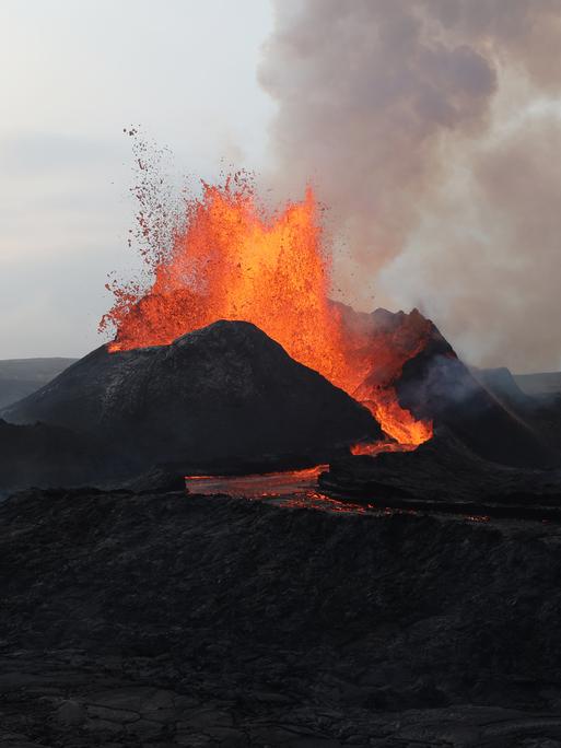Ein Vulkanausbruch, die Lavawolke steigt auf und läuft am Berg herunter.