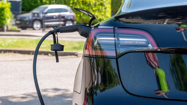 Ein dunkles Elektroauto mit eingestecktem, schwarzem Ladestecker, parkt zum Aufladen auf einem E-Parkplatz.