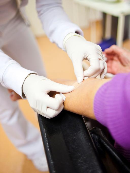 Nahaufnahme einer Blutabnahme in einer Arztpraxis. Das Pflaster nach der Blutentnahme wird auf den Arm geklebt Nahaufnahme einer Blutabnahme in einer Arztpraxis. Das Pflaster nach der Blutentnahme wird auf den Arm geklebt