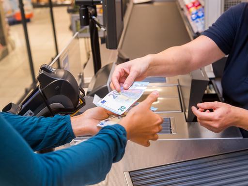 Bezahlen an der Supermarktkasse: Nahaufnahme der Hände mit Geldscheinen