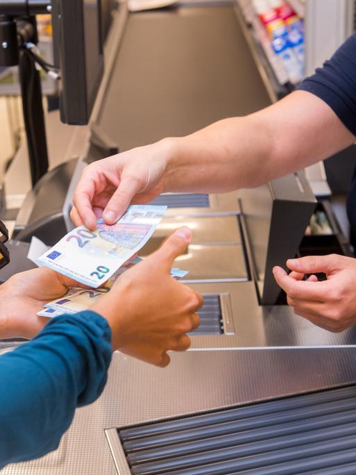 Bezahlen an der Supermarktkasse: Nahaufnahme der Hände mit Geldscheinen