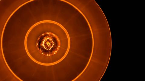 Blick auf eine Glühbirne in tellerförmiger Lampe, die rostrot-orangenes Licht in eine schwarze Umgebung abgiebt.