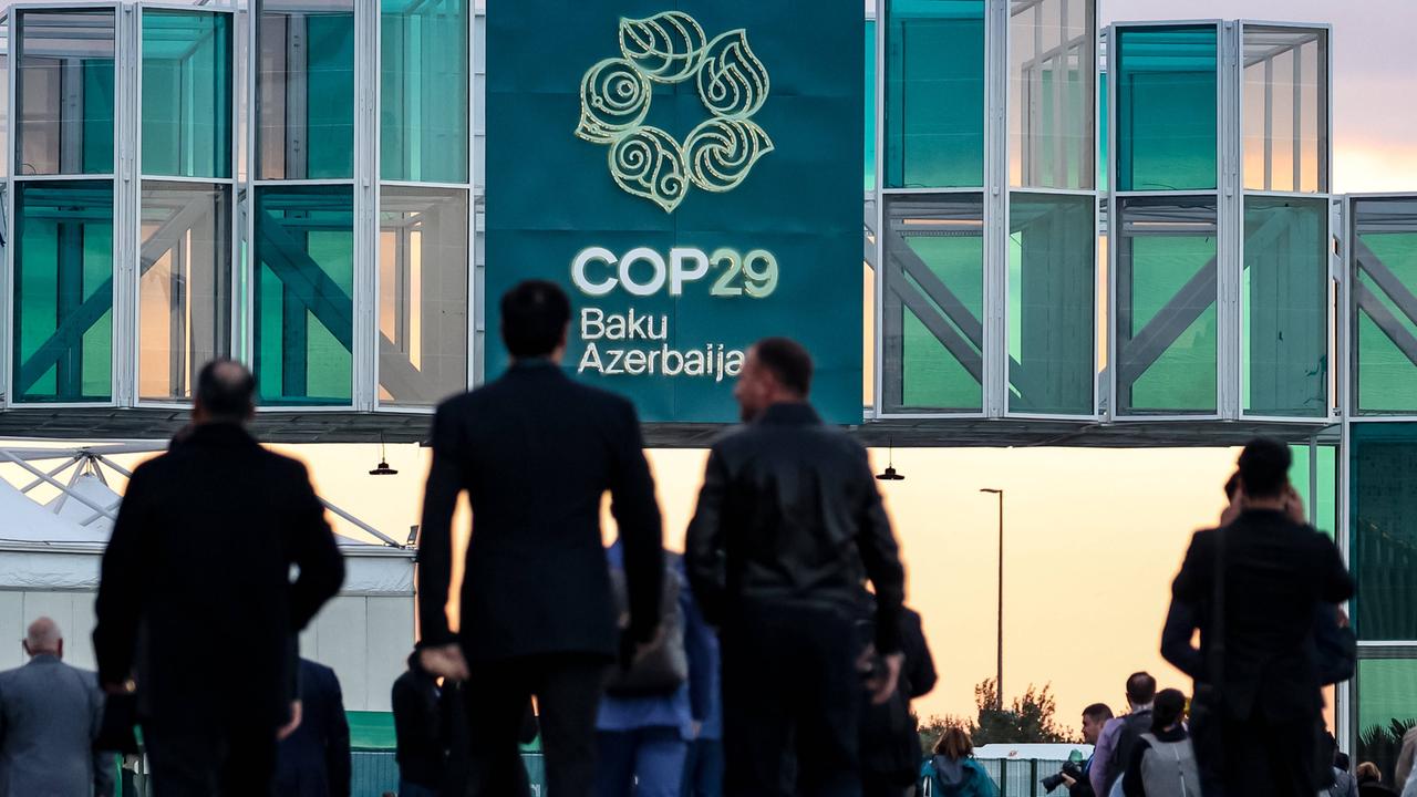 Besucher der Weltklimakonferenz in Baku laufen auf den Eingang einer Konferenzhalle zu.