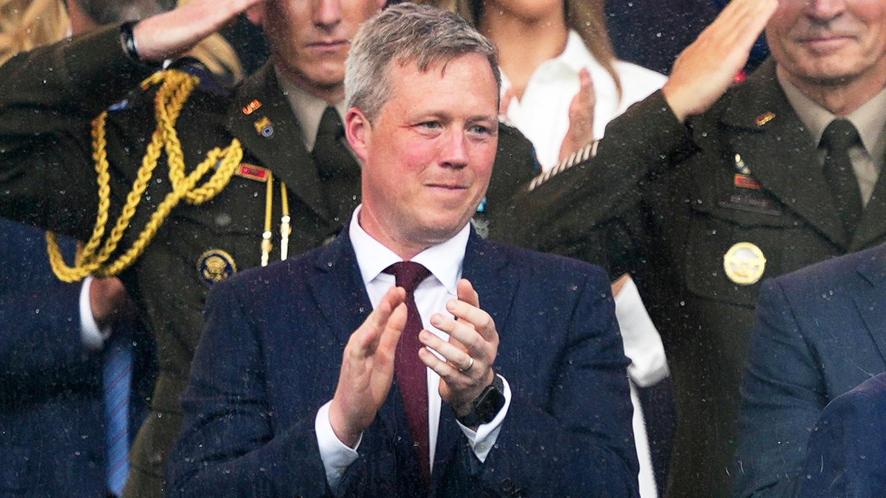 Daniel Driscoll steht im Anzug mit Krawatte auf einer Tribüne und klatsch. Um ihn herum sind viele weitere Menschen zu sehen, bei denen es sich vorwiegend um Militärs in Uniform handelt. Daniel Driscoll steht im Anzug mit Krawatte auf einer Tribüne und klatsch. Um ihn herum sind viele weitere Menschen zu sehen, bei denen es sich vorwiegend um Militärs in Uniform handelt.