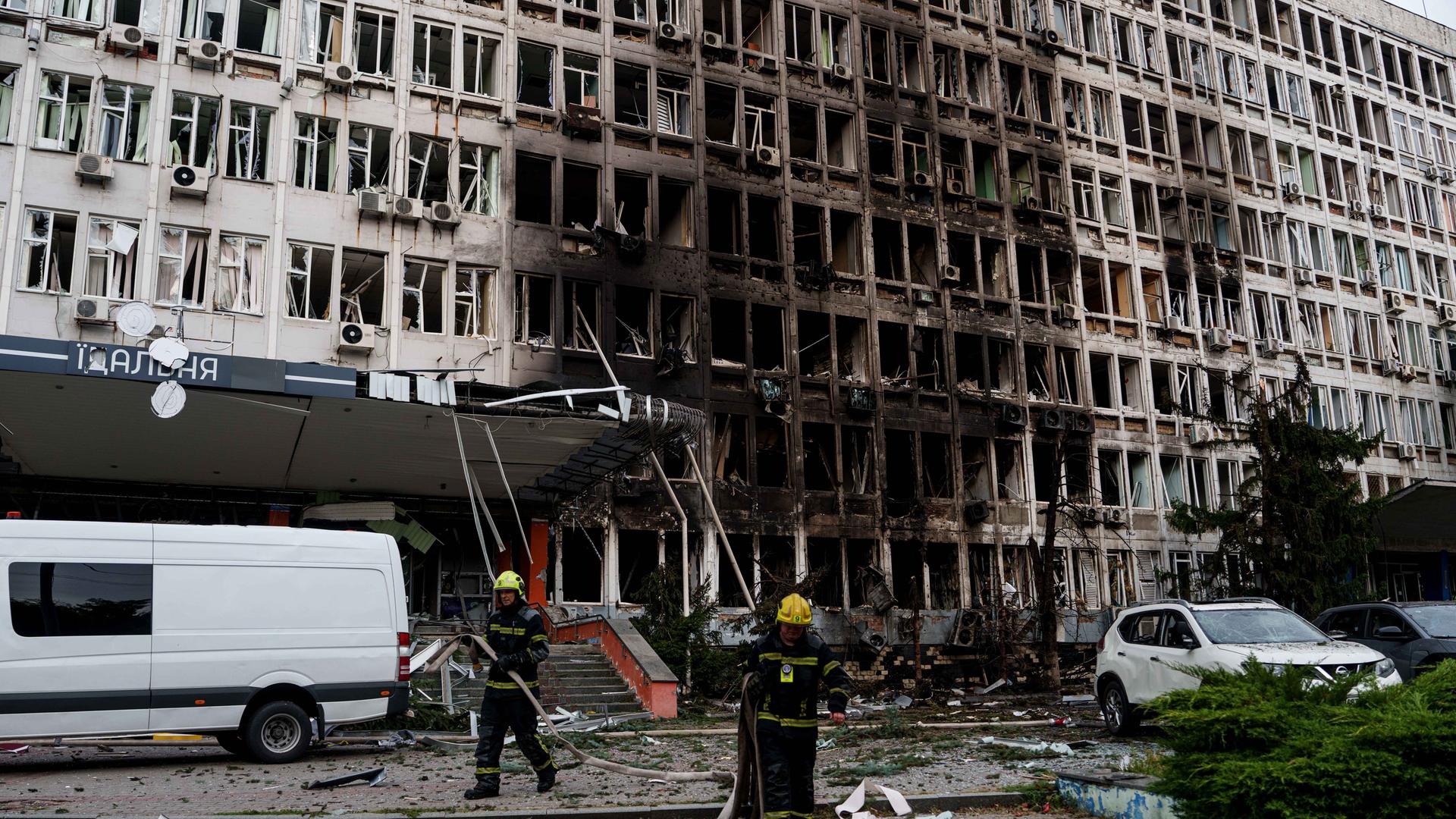 Rettungskräfte rollen vor einem Bürogebäude, das durch einen russischen Drohnenangriff beschädigt wurde, Feuerwehrschläuche auf. 