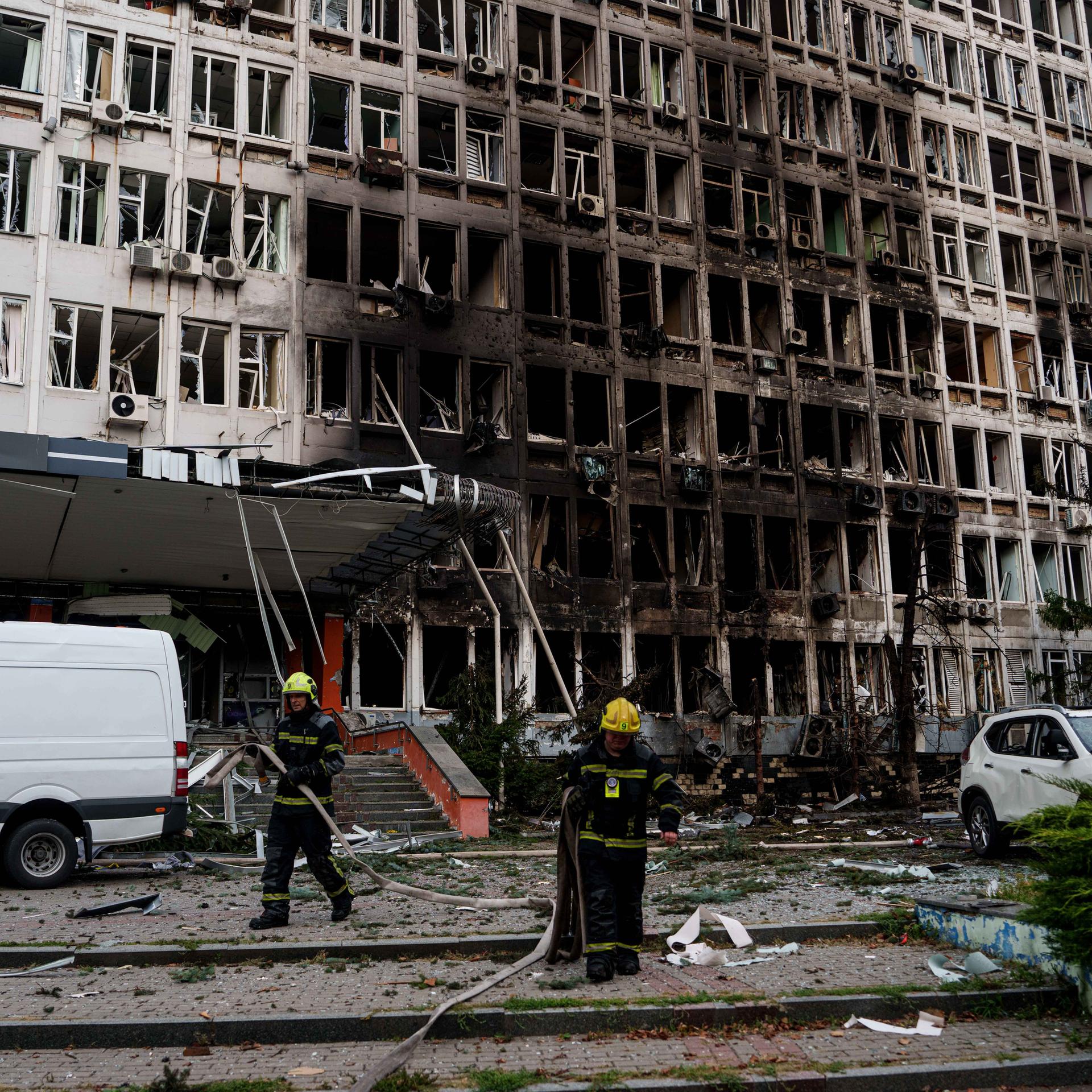 Rettungskräfte rollen vor einem Bürogebäude, das durch einen russischen Drohnenangriff beschädigt wurde, Feuerwehrschläuche auf. 
