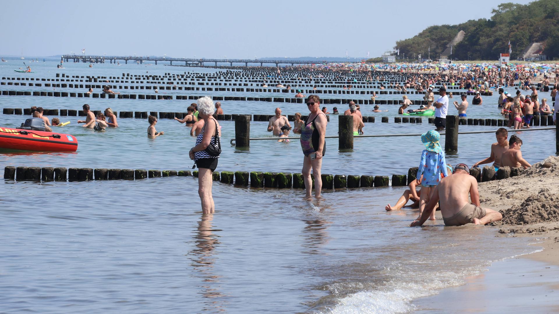 Zahlreiche Menschen am Strand, einige stehen mit den Füßen im Meer Zahlreiche Menschen am Strand, einige stehen mit den Füßen im Meer