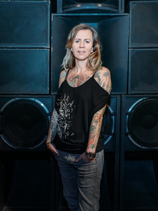 Pamela Schobeß, Clubbetreiberin und Vorsitzende der Clubcommission Berlin, steht vor einer Wand aus riesigen Lautsprechern.