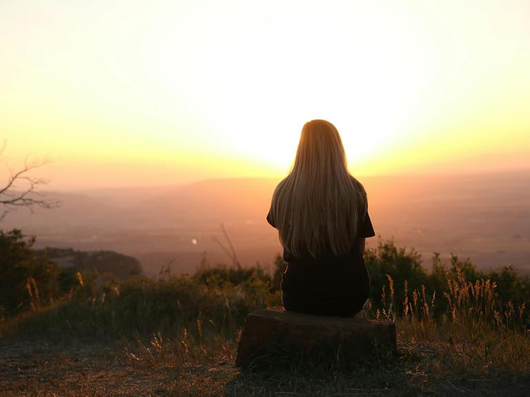 Eine Frau schaut in den Sonnenaufgang.