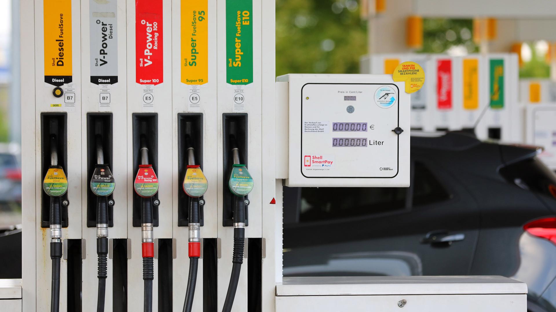 An einer Tankstelle hängen die Zapfhähne für Diesel und Benzin nebeneinander an der Zapfsäule. Im Hintergund steht ein grauer PKW. An einer Tankstelle hängen die Zapfhähne für Diesel und Benzin nebeneinander an der Zapfsäule. Im Hintergund steht ein grauer PKW.