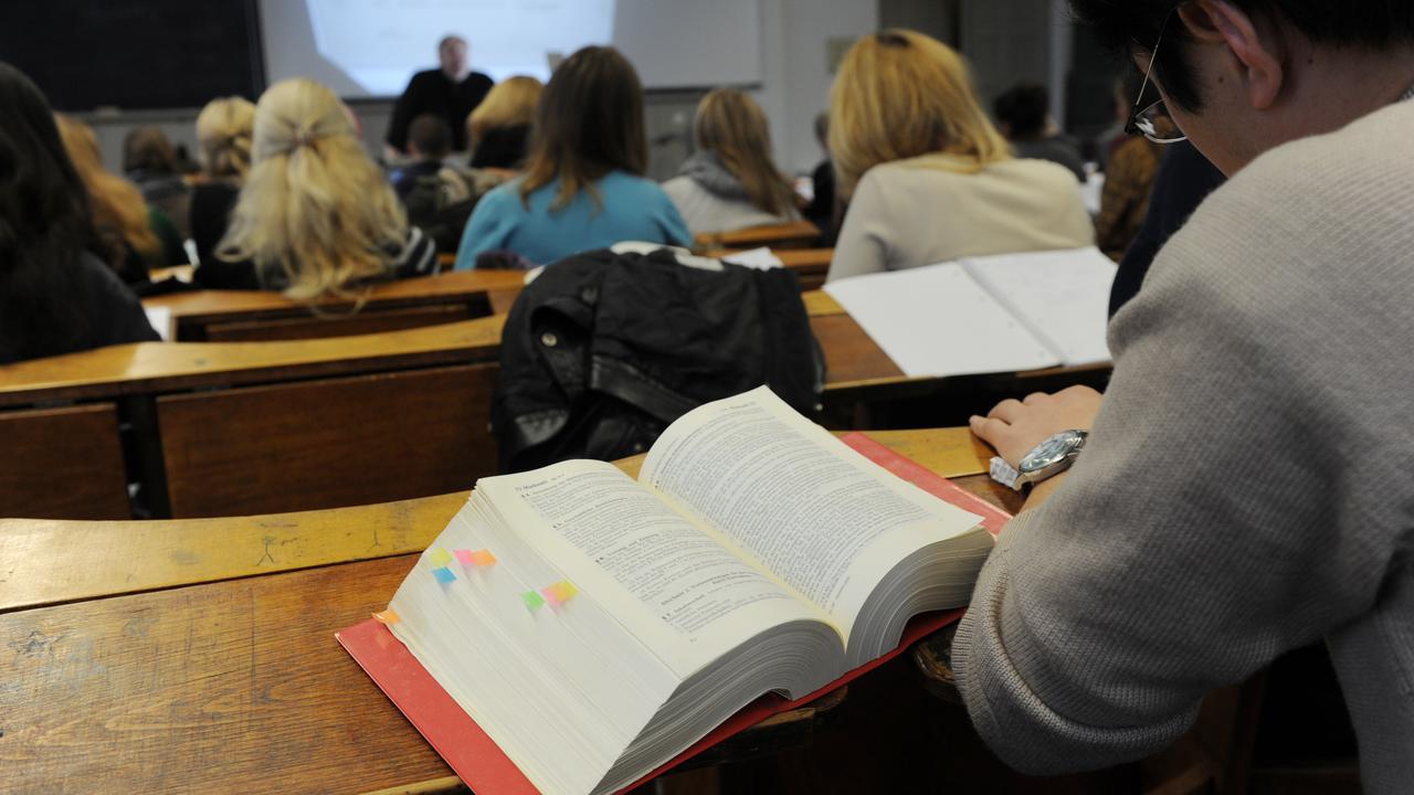 Studierende sitzen in einer juristischen Vorlesung in einem Hörsaal. Man erkennt unten am Pult einen Dozenten und neben dem Student ein aufgeschlagenes Gesetzbuch.