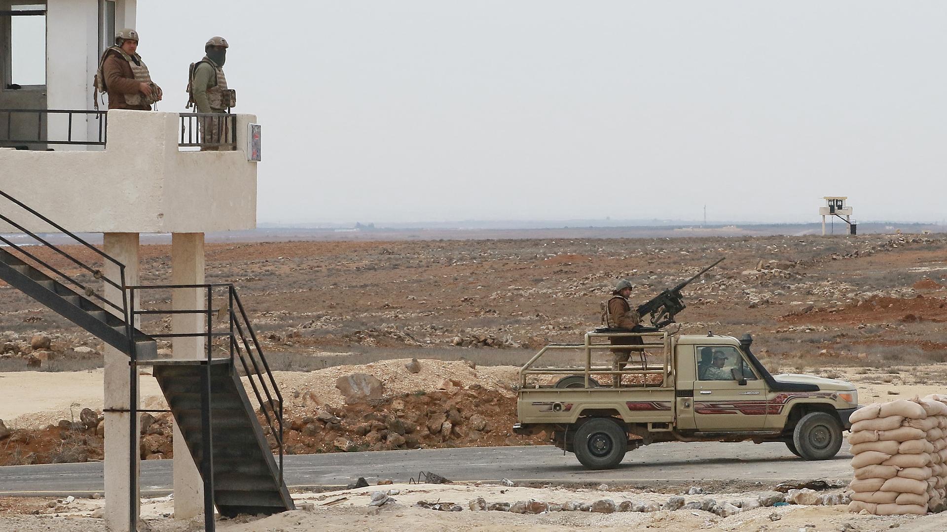 Ein Wachturm, auf dem zwei Soldaten stehen und ein Armeejeep, auf dem ein Soldaten mit einem Gewehr steht, patrouillieren an der syrisch-jordanischen Grenze.