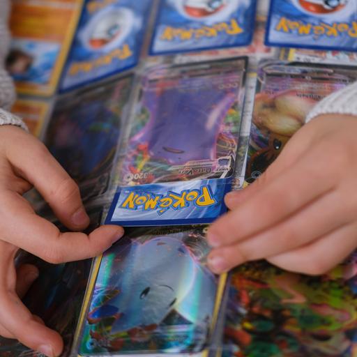 Man sieht einige Pokemon-Karten in einem Sammelalbum und Kinderhände, die eine Karte halten.
