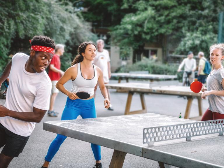 Eine Gruppe junger Leute spielt im Kreis rennend Tischtennis.