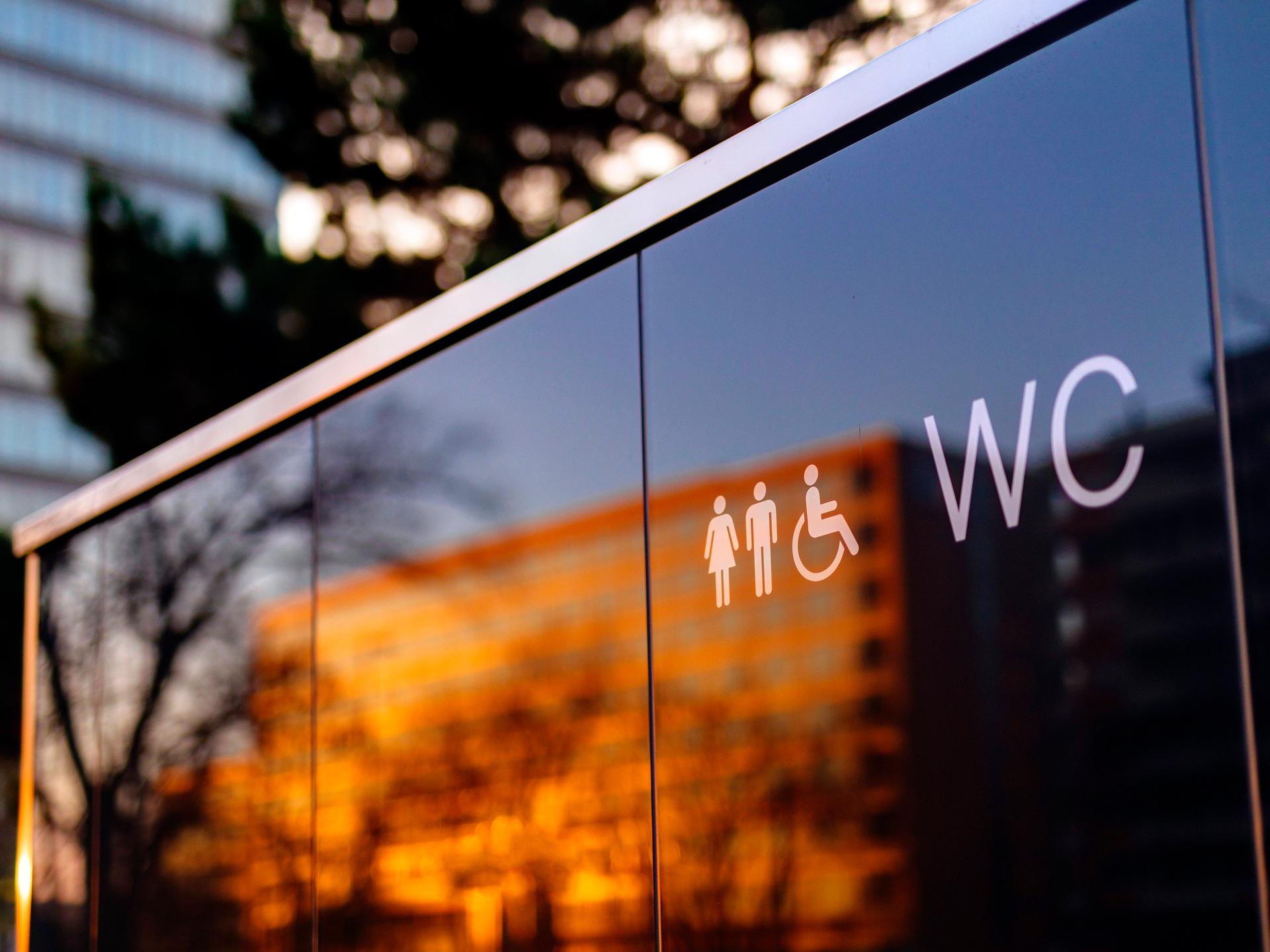 Öffentliche Toilette in Deutz. In der Glasfront des Häuschens spiegelt sich ein gegenüberliegender Wohnblock.
