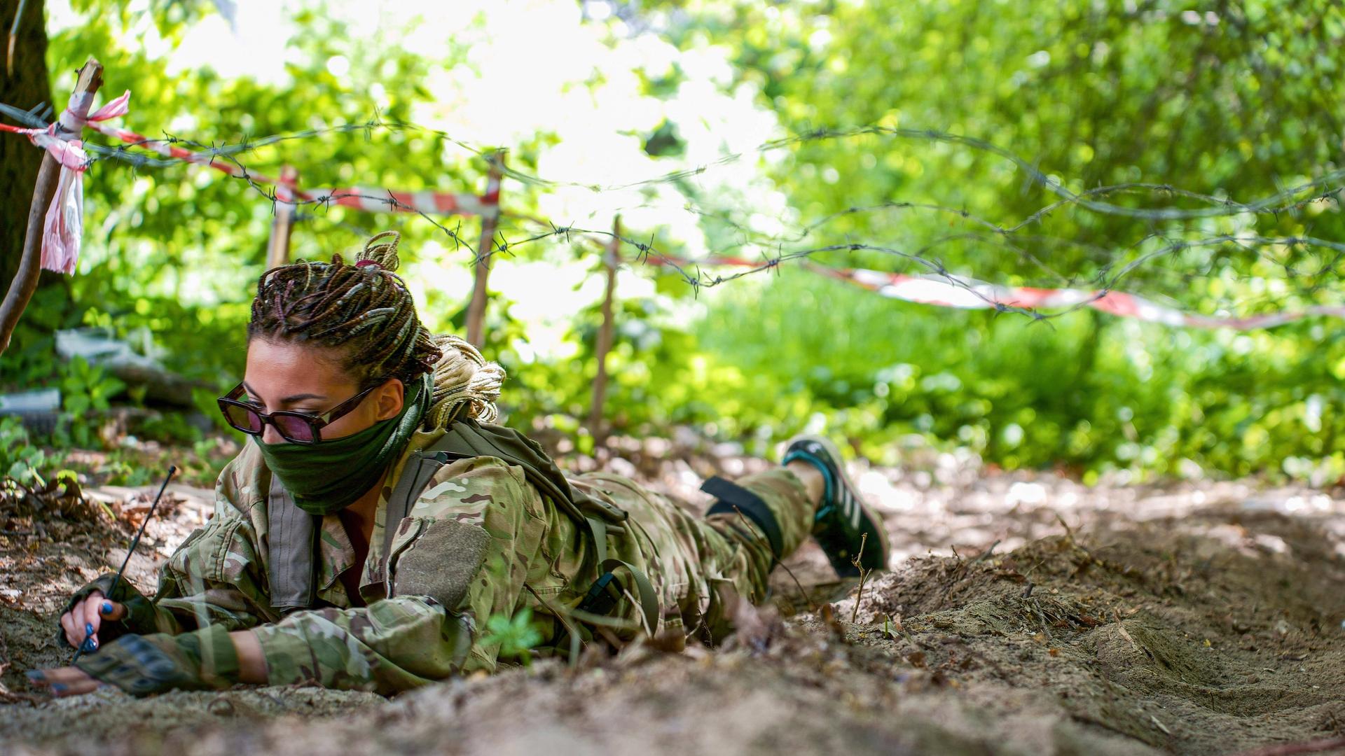 Eine ukrainische Soldatin entschärft auf dem Boden liegend eine russische Landmine. 