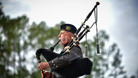 Ein Schotte spielt Dudelsack. Man sieht ihn im Profil, während die Pfeifen in den Himmel ragen.