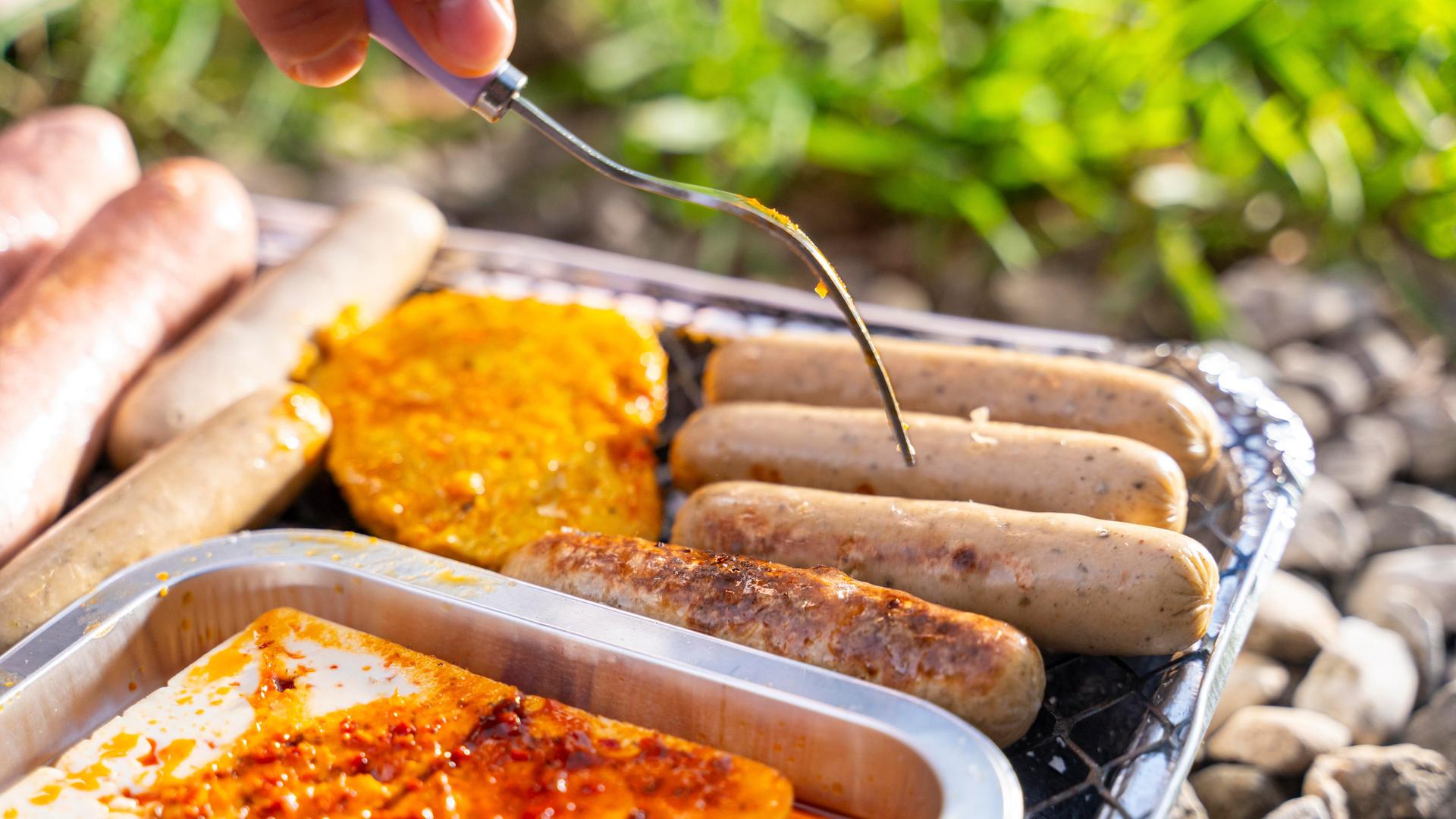 Vegetarische und vegane Würstchen und Bratlinge auf einem Grill.