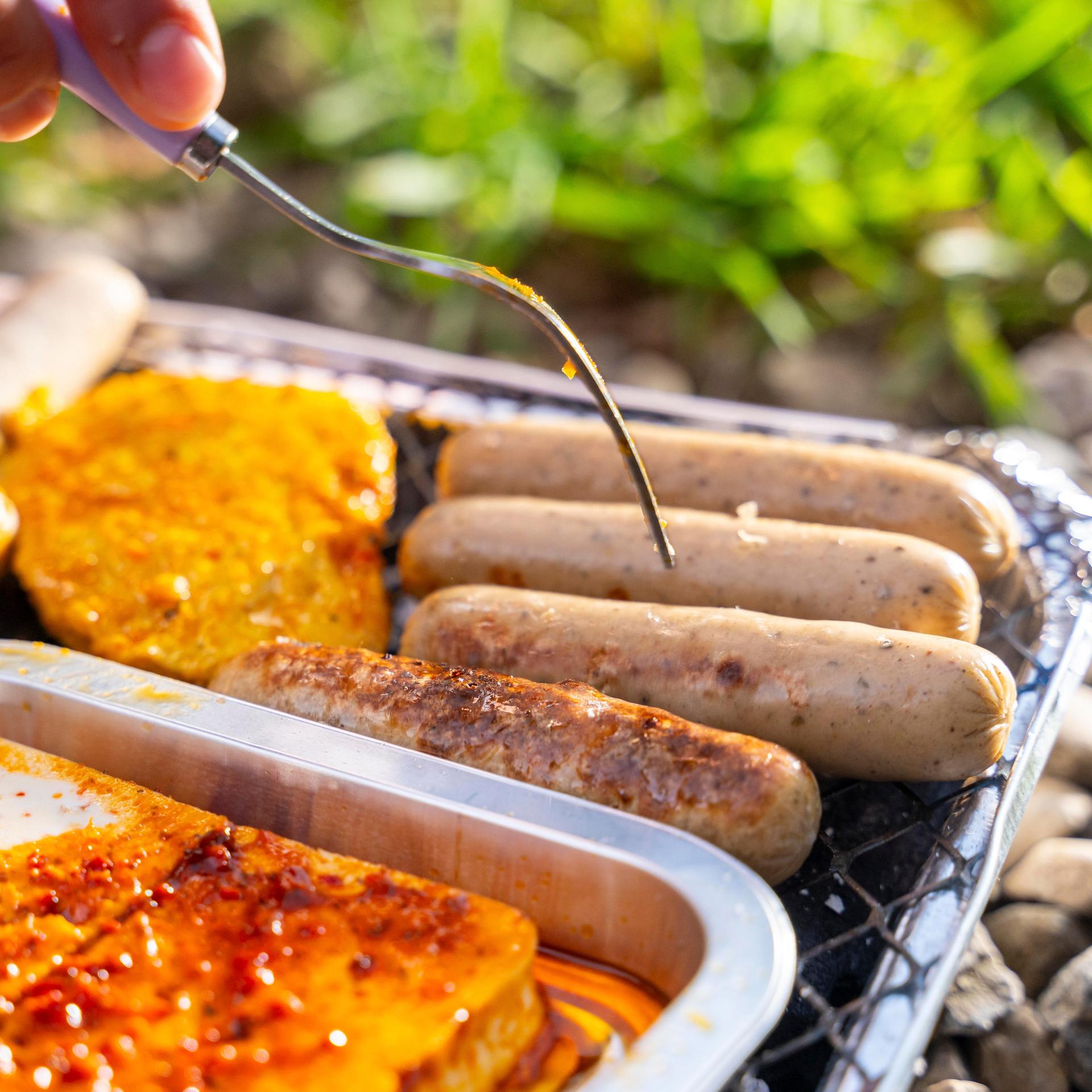 Vegetarische und vegane Würstchen und Bratlinge auf einem Grill.