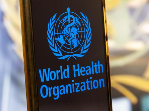 Symbolbild: Smartphone mit Logo der WHO (World Health Organisation) vor einem unscharfen Hintergrund