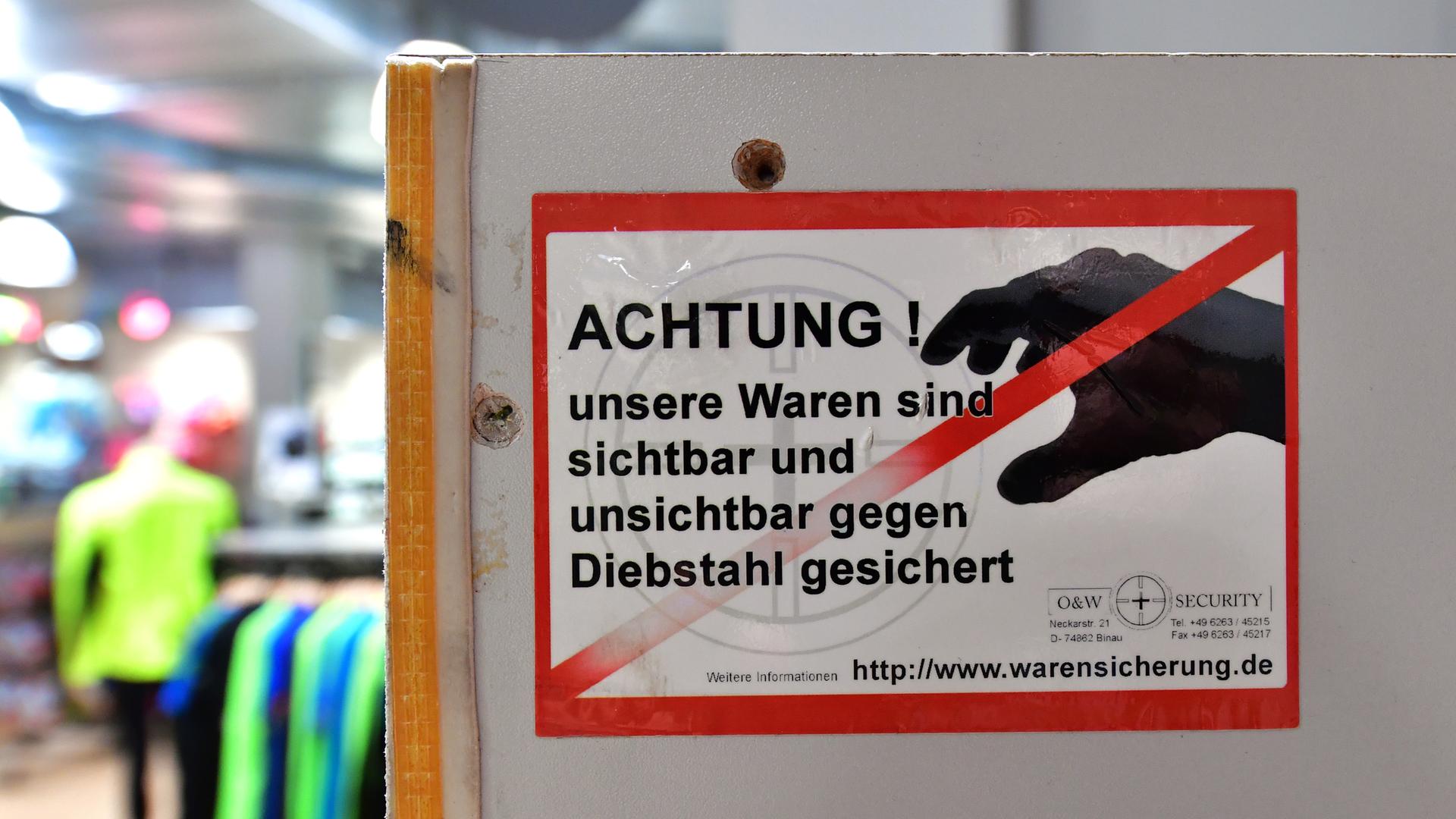 Ein Aufkleber mit der Aufschrift "Achtung ! unsere Waren sind sichtbar und unsichtbar gegen Diebstahl gesichert" ist an der Umkleidekabine in einem Sportgeschäft zu sehen. 