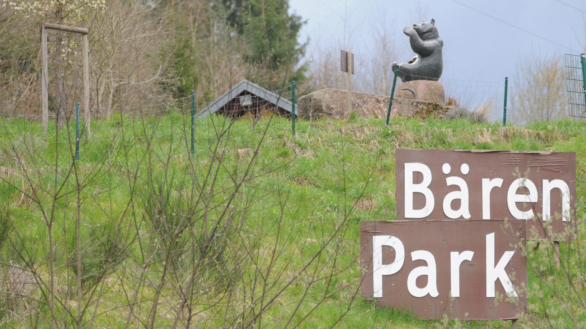Blick auf einen Hügel und ein Schild mit dem Schriftzug "Bärenpark". Im Hintergrund die Statue eines Bären.
