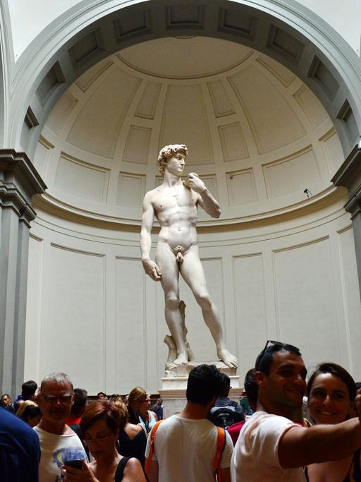 Der David von Michelangelo in der Galleria dell Accademia in Florenz. Vor der Statue stehen viele Besucher, einige machen mit ihren Handys Fotos.