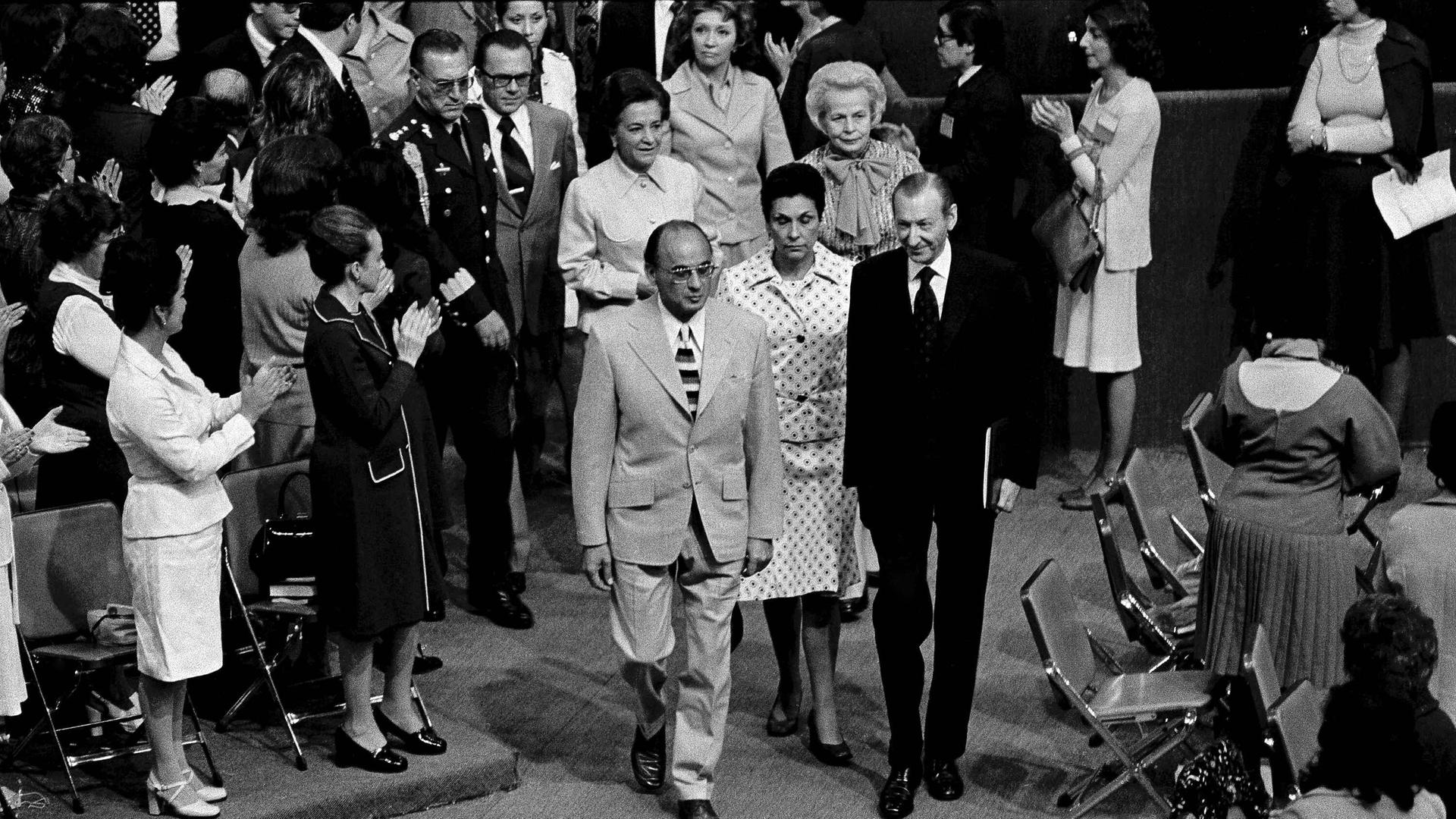 Damaliger UN-Generalsekretär Kurt Waldheim (rechts) und Mexikos Präsident Luis Echeverria gehen durch stehende Menschen bei der Eröffnung der Konferenz. Hinter den beiden ist Helvi Sipilä, die die Konferenz leitete.