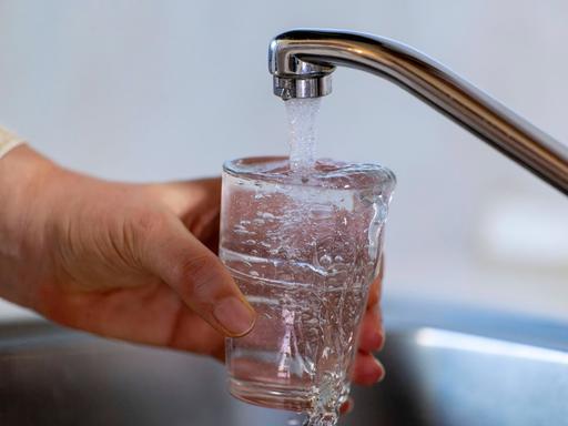 Eine Hand hält ein Glas unter einem Wasserhahn. 