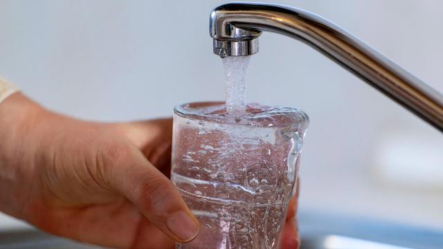 Eine Hand hält ein Glas unter einem Wasserhahn. 