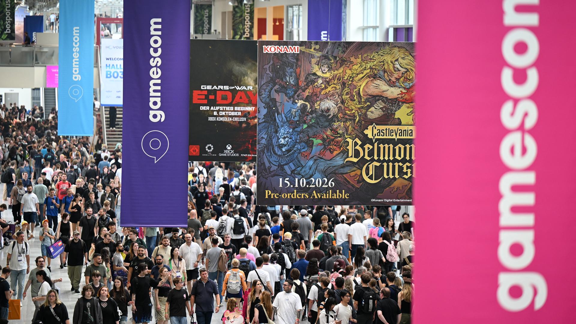 Besucher gehen am zweiten Tag der diesjährigen Computer- und Videospiel-Messe Gamescom durch einen Flur, von der Decke hängen Gamescom-Logos herab.