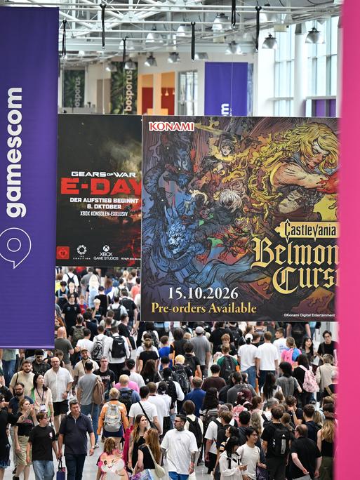 Besucher gehen am zweiten Tag der diesjährigen Computer- und Videospiel-Messe Gamescom durch einen Flur, von der Decke hängen Gamescom-Logos herab.