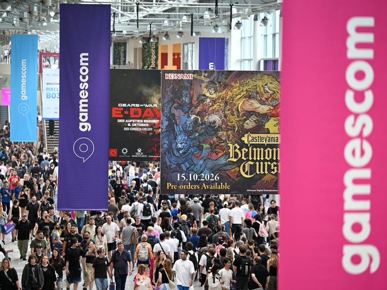 Besucher gehen am zweiten Tag der diesjährigen Computer- und Videospiel-Messe Gamescom durch einen Flur, von der Decke hängen Gamescom-Logos herab.