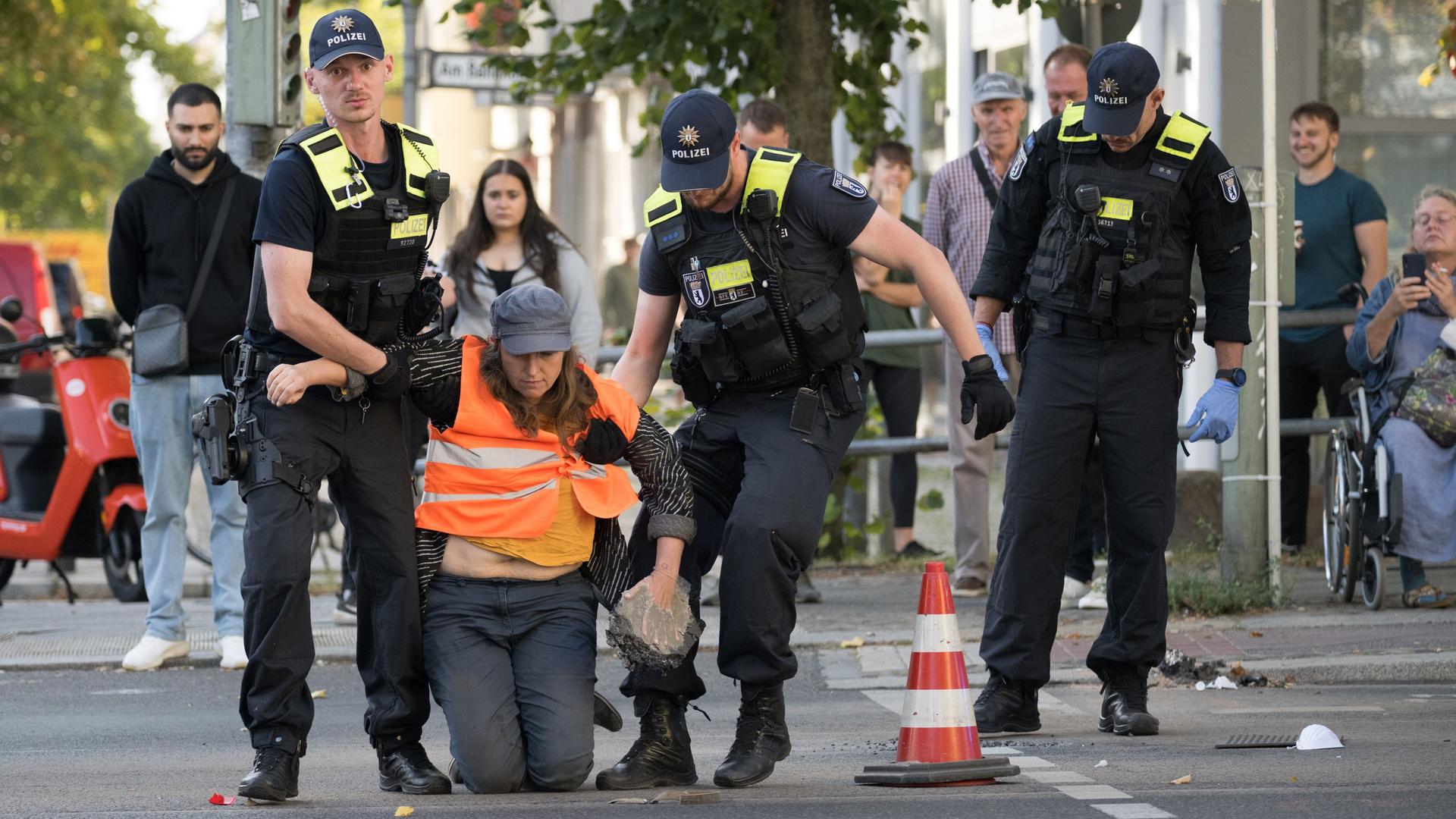 Berlin: Eine Aktivistin der Klimaschutzgruppe "Letzte Generation" wird von Polizeibeamten am Spandauer Damm über die Straße getragen, nachdem sie mit schwerem Gerät befreit werden musste.