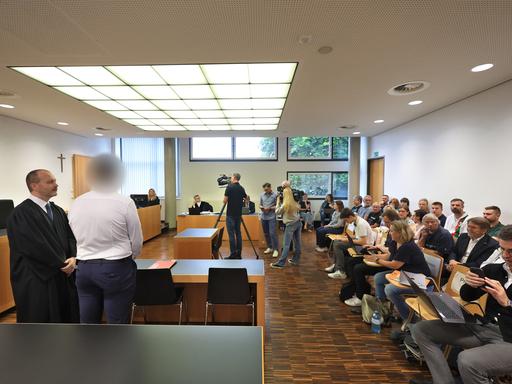 Ein Polizist (M) steht in einem Gerichtssaal im Landgericht neben seinem Anwalt.