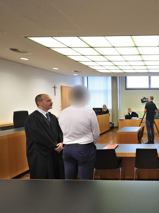 Ein Polizist (M) steht in einem Gerichtssaal im Landgericht neben seinem Anwalt.