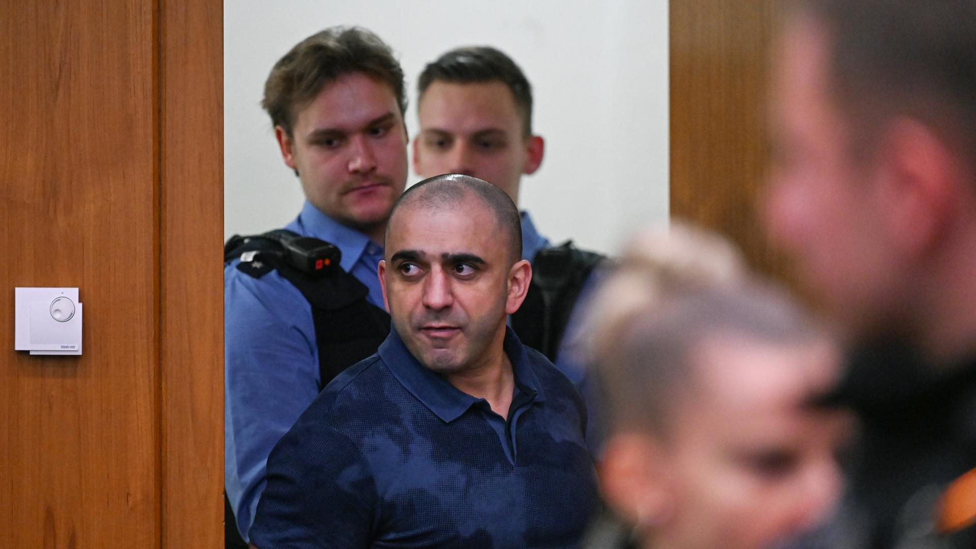 Ein Angeklagter wird von Polizisten in den Gerichtssaal geführt. Ein Angeklagter wird von Polizisten in den Gerichtssaal geführt.