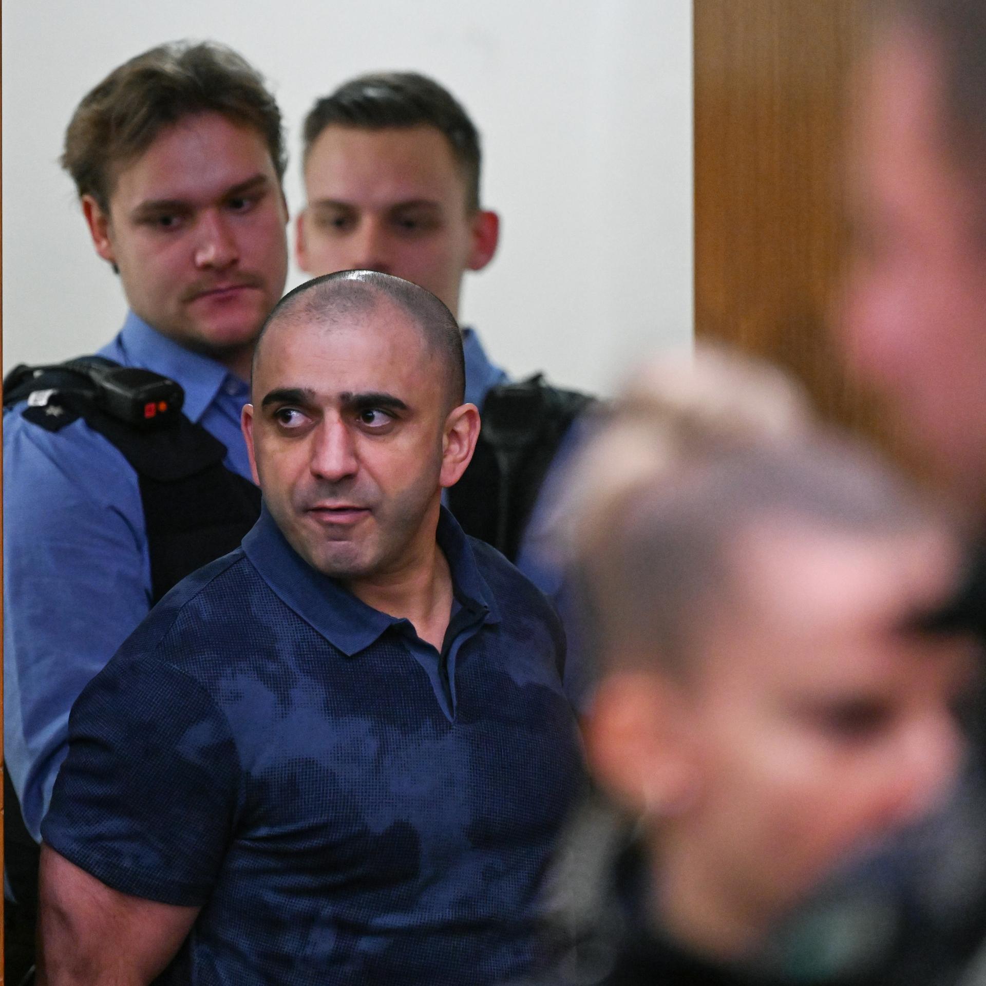 Ein Angeklagten wird von Polizisten in den Gerichtssaal geführt. 