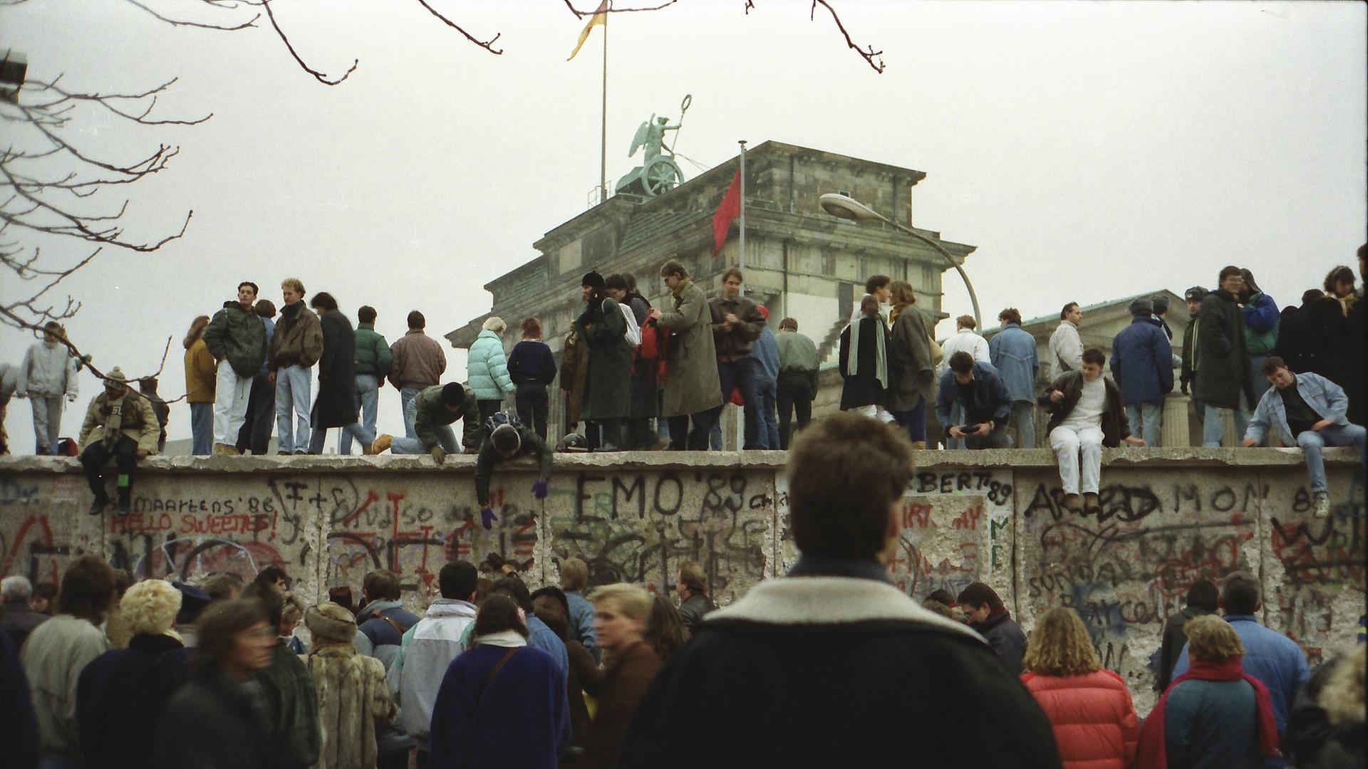 Menschen stehen vor und auf der Mauer am Brandenburger Tor nach der Wende vom 9. November 1989.