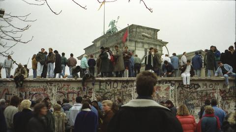 Menschen stehen vor und auf der Mauer am Brandenburger Tor nach der Wende vom 9. November 1989.