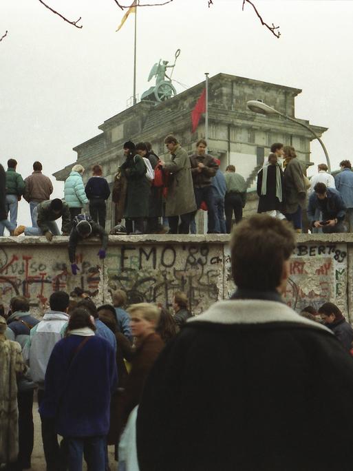 Menschen stehen vor und auf der Mauer am Brandenburger Tor nach der Wende vom 9. November 1989.