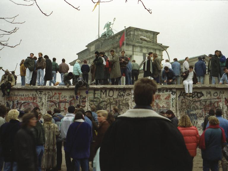 Menschen stehen vor und auf der Mauer am Brandenburger Tor nach der Wende vom 9. November 1989.
