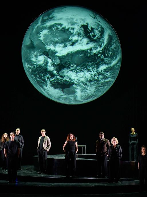 Szenenfoto aus der Produktion "Wir sind das Volk" am Deutschen Nationaltheater Weimar: Schauspielende auf einer dunklen Bühne blicken Richtung Publikum, hinter ihnen eine Projektion der Erdkugel. Szenenfoto aus der Produktion "Wir sind das Volk" am Deutschen Nationaltheater Weimar: Schauspielende auf einer dunklen Bühne blicken Richtung Publikum, hinter ihnen eine Projektion der Erdkugel.