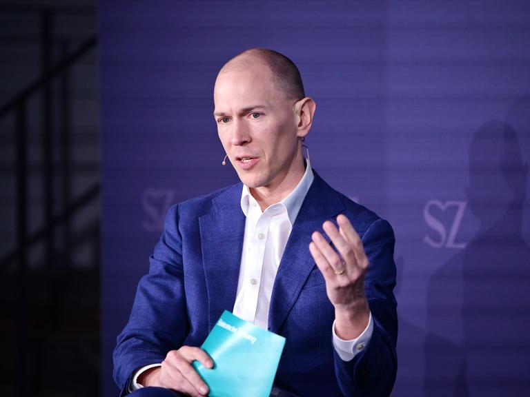 Jannis Brühl sitzt beim Digitalgipfel der "Süddeutschen Zeitung" auf dem Podium und gestikuliert beim Sprechen. Jannis Brühl sitzt beim Digitalgipfel der "Süddeutschen Zeitung" auf dem Podium und gestikuliert beim Sprechen.
